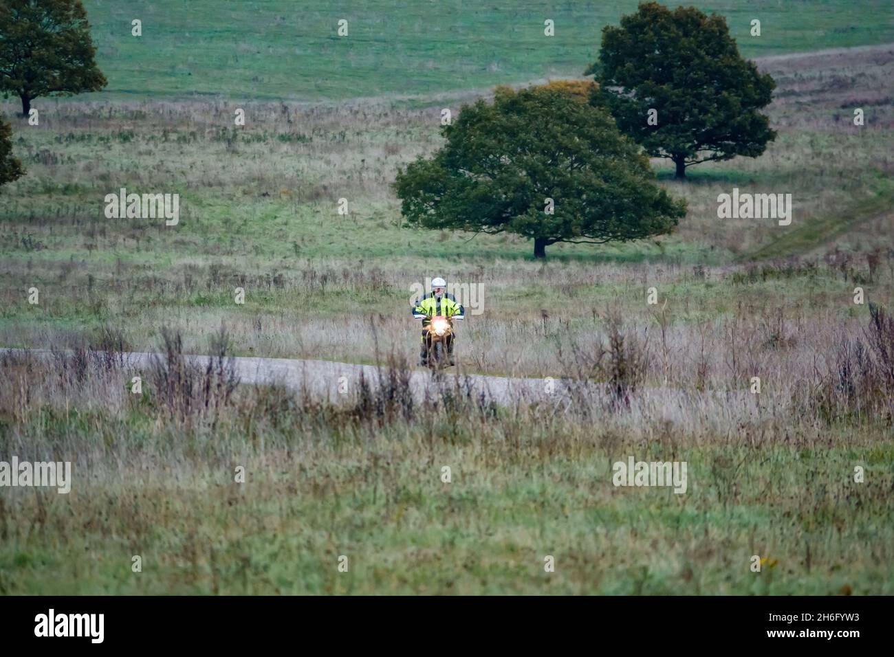 Un motociclista (motociclista) in una giacca gialla ad alta visibilità che guida la sua moto lungo una pista di pietra sulla Salisbury Plain, Wiltshire Foto Stock