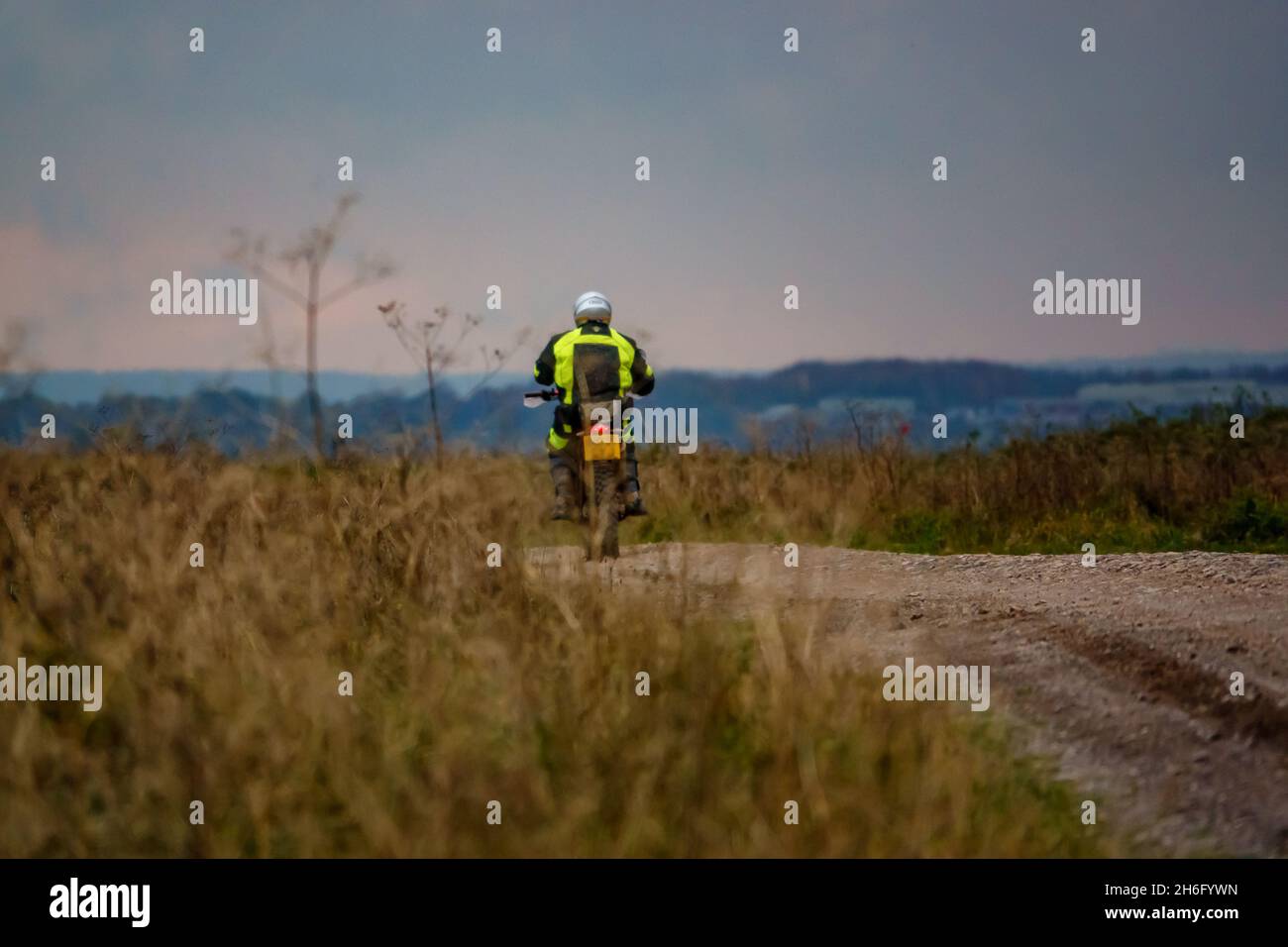 Un motociclista (motociclista) in una giacca gialla ad alta visibilità che guida la sua moto lungo una pista di pietra sulla Salisbury Plain, Wiltshire Foto Stock