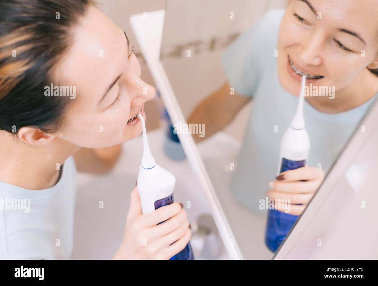 Donna con bretelle sui denti spazzolando i denti con utilizzando un irrigato, prima specchio, vista dall'alto. Foto Stock