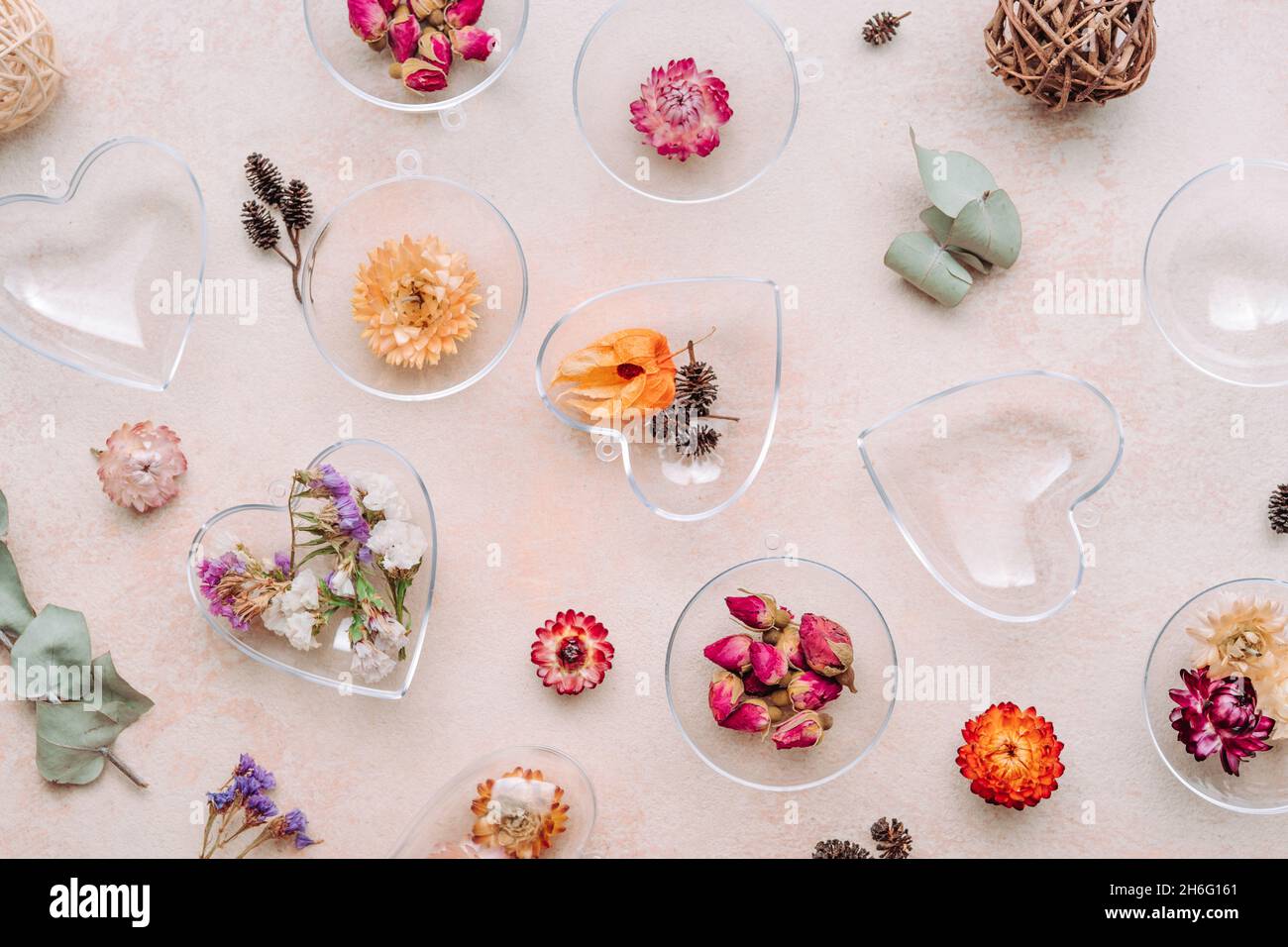 Ornamenti fai-da-te riempiti di fiori secchi su fondo di cemento beige. Albero di Natale o idea di decorazione di San Valentino. Vista dall'alto, piatto Foto Stock