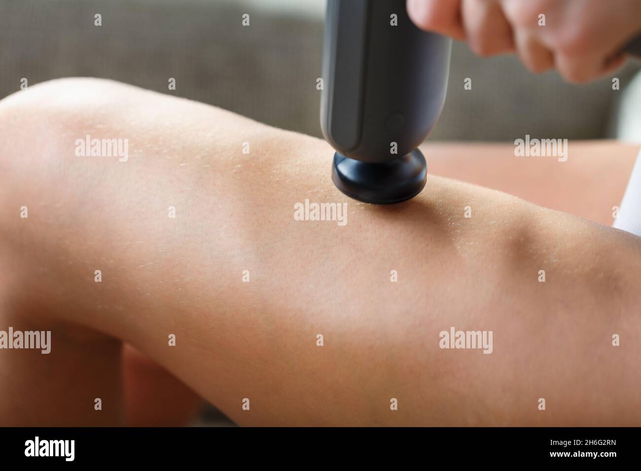 Auto-massaggio delle gambe delle donne con una pistola perfezionante a casa. Massaggio antiurto per ripristinare i muscoli della plancia e i punti di attivazione Foto Stock