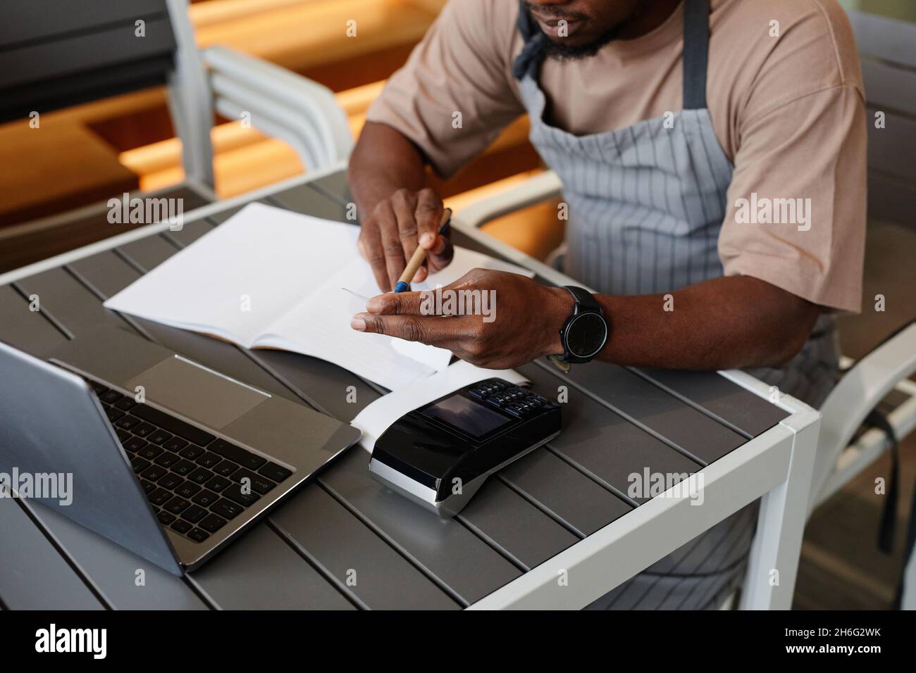 Scatto ad alta angolazione di un giovane irriconoscibile seduto al tavolo di fronte al laptop in un moderno piccolo bar che prende gli ordini online per la consegna Foto Stock