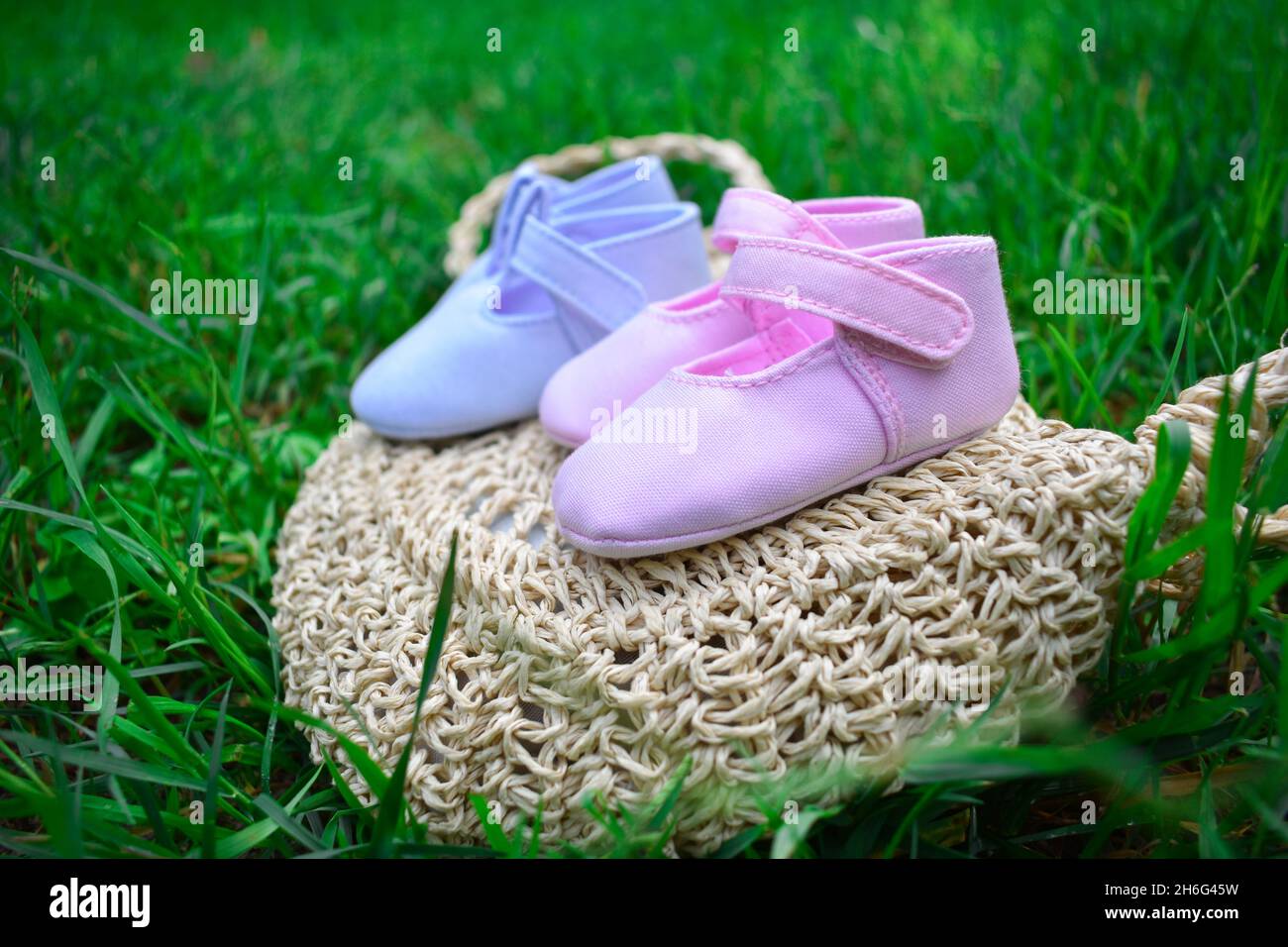 Scarpe per bambini rosa e blu su un sacchetto di vimini su erba verde fresca Foto Stock