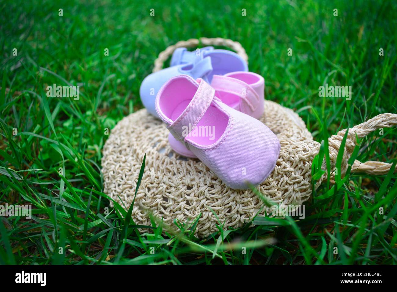 Scarpe per bambini rosa e blu su un sacchetto di vimini su erba verde fresca Foto Stock