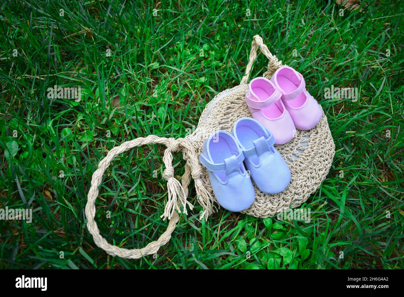 Scarpe per bambini rosa e blu su un sacchetto di vimini su erba verde fresca Foto Stock