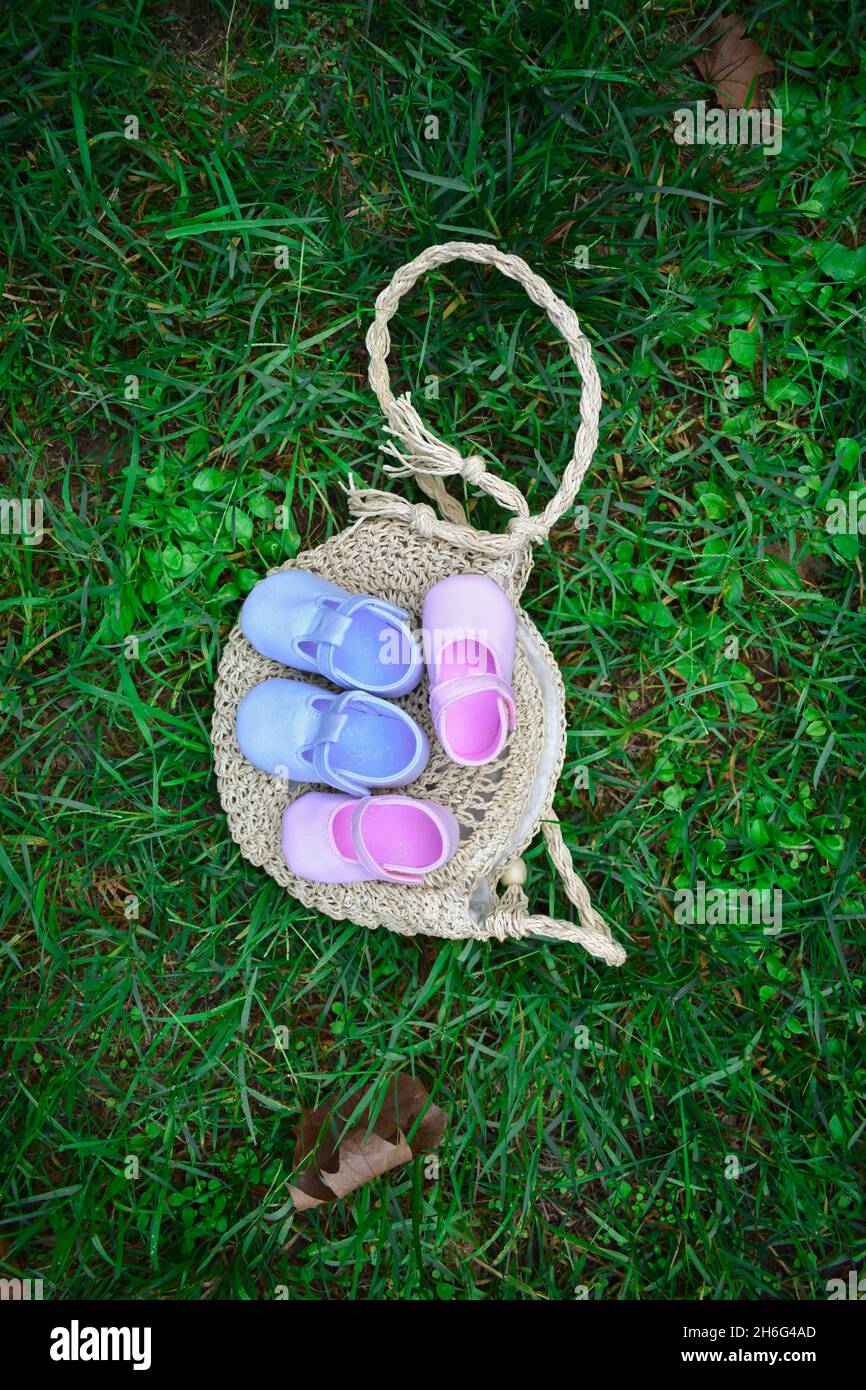 Scarpe per bambini rosa e blu su un sacchetto di vimini su erba verde fresca Foto Stock