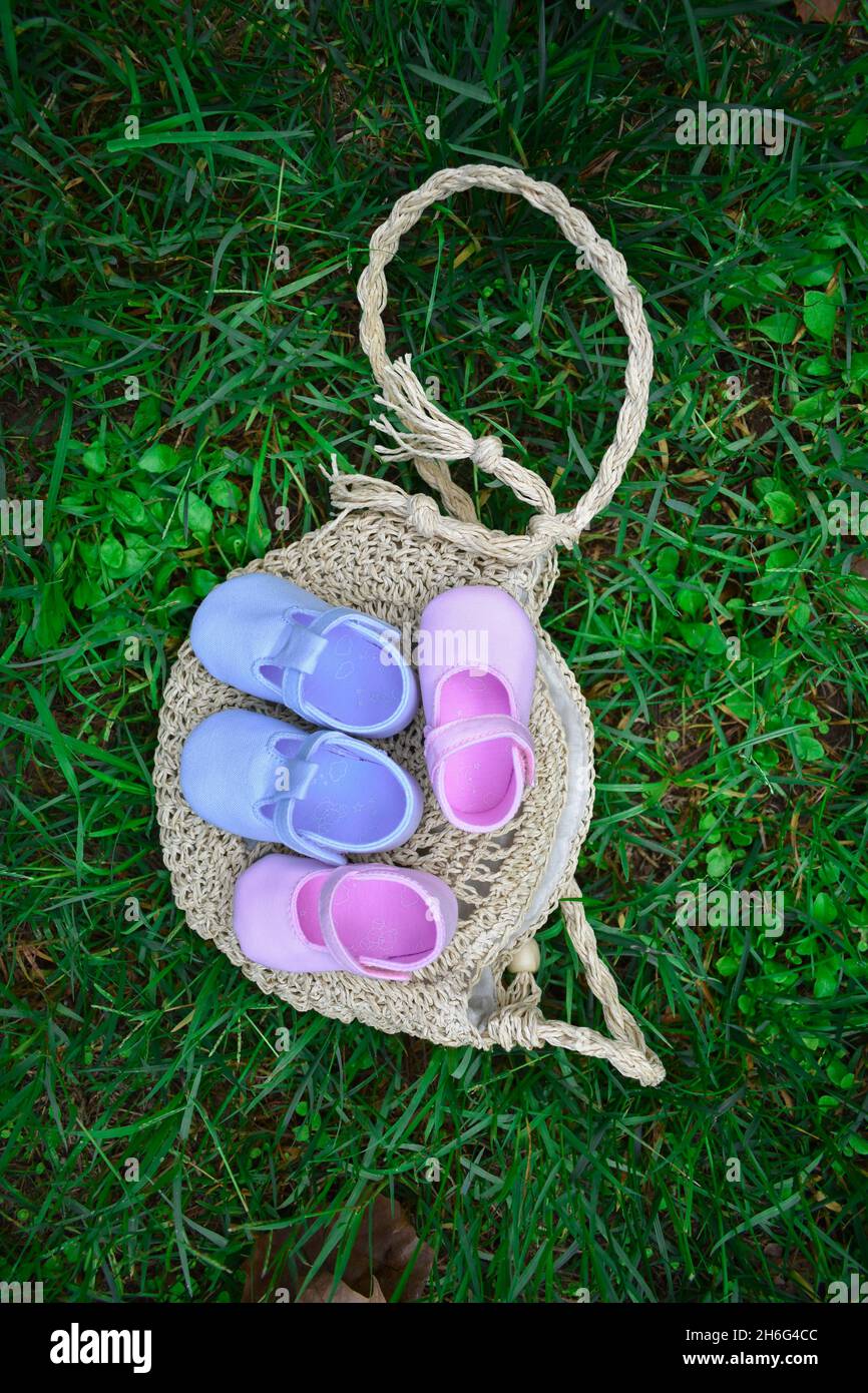 Scarpe per bambini rosa e blu su un sacchetto di vimini su erba verde fresca Foto Stock