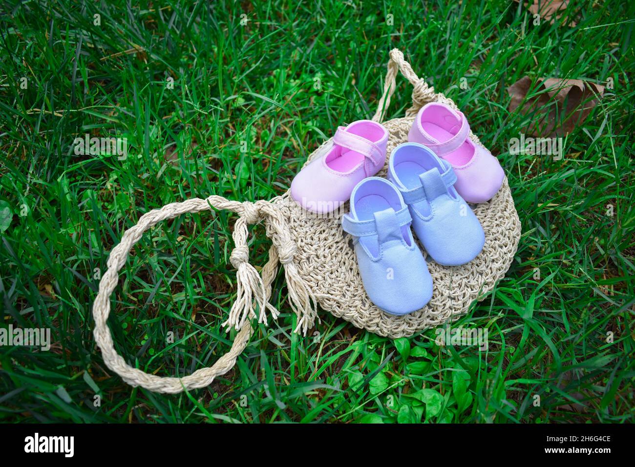 Scarpe per bambini rosa e blu su un sacchetto di vimini su erba verde fresca Foto Stock