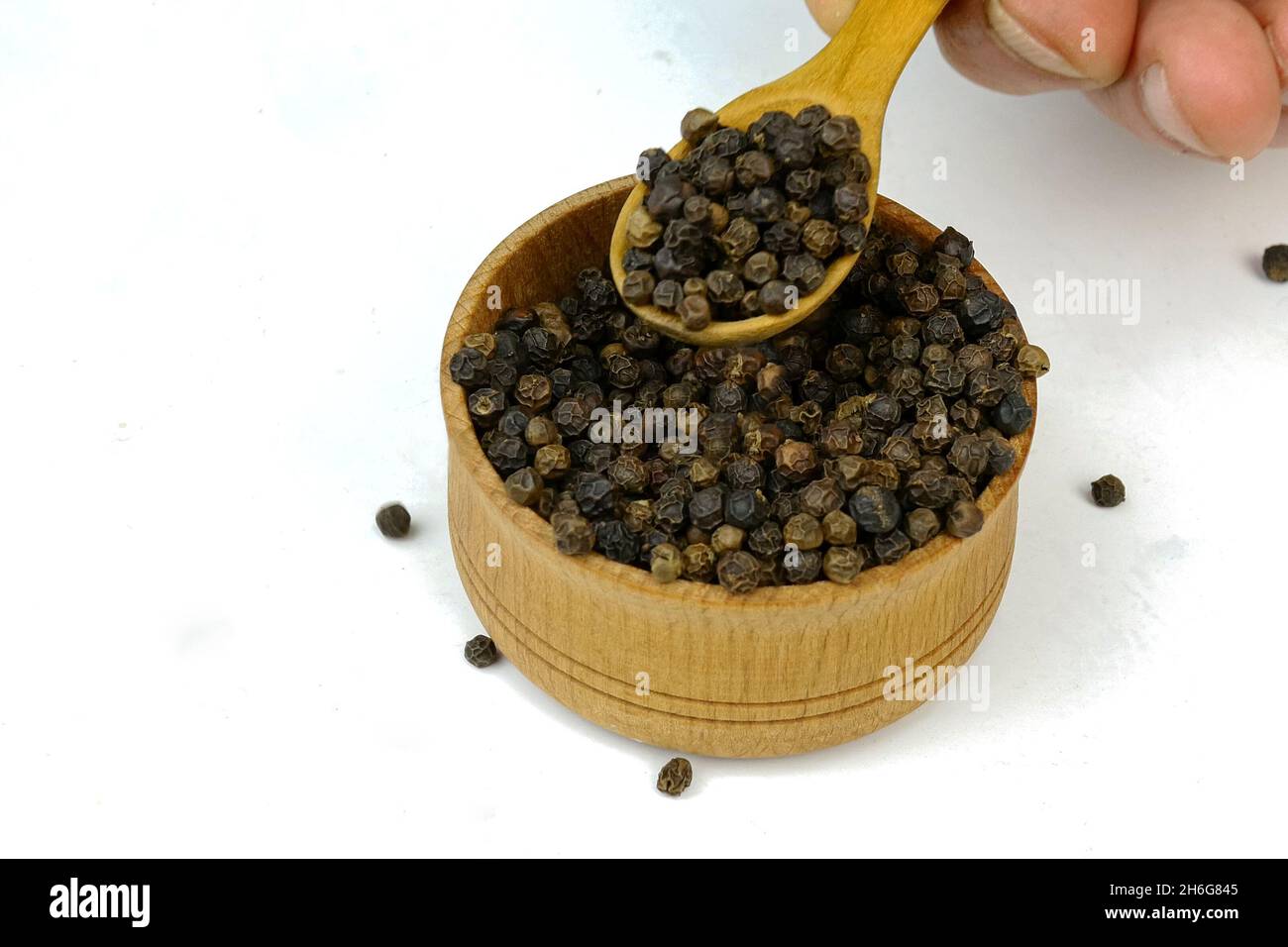 Chef che prende le spezie secche pepe nero corna e dal vaso speziato in legno. Messa a fuoco selettiva. Concentratevi sulle spezie nel vaso. Primo piano. Foto Stock