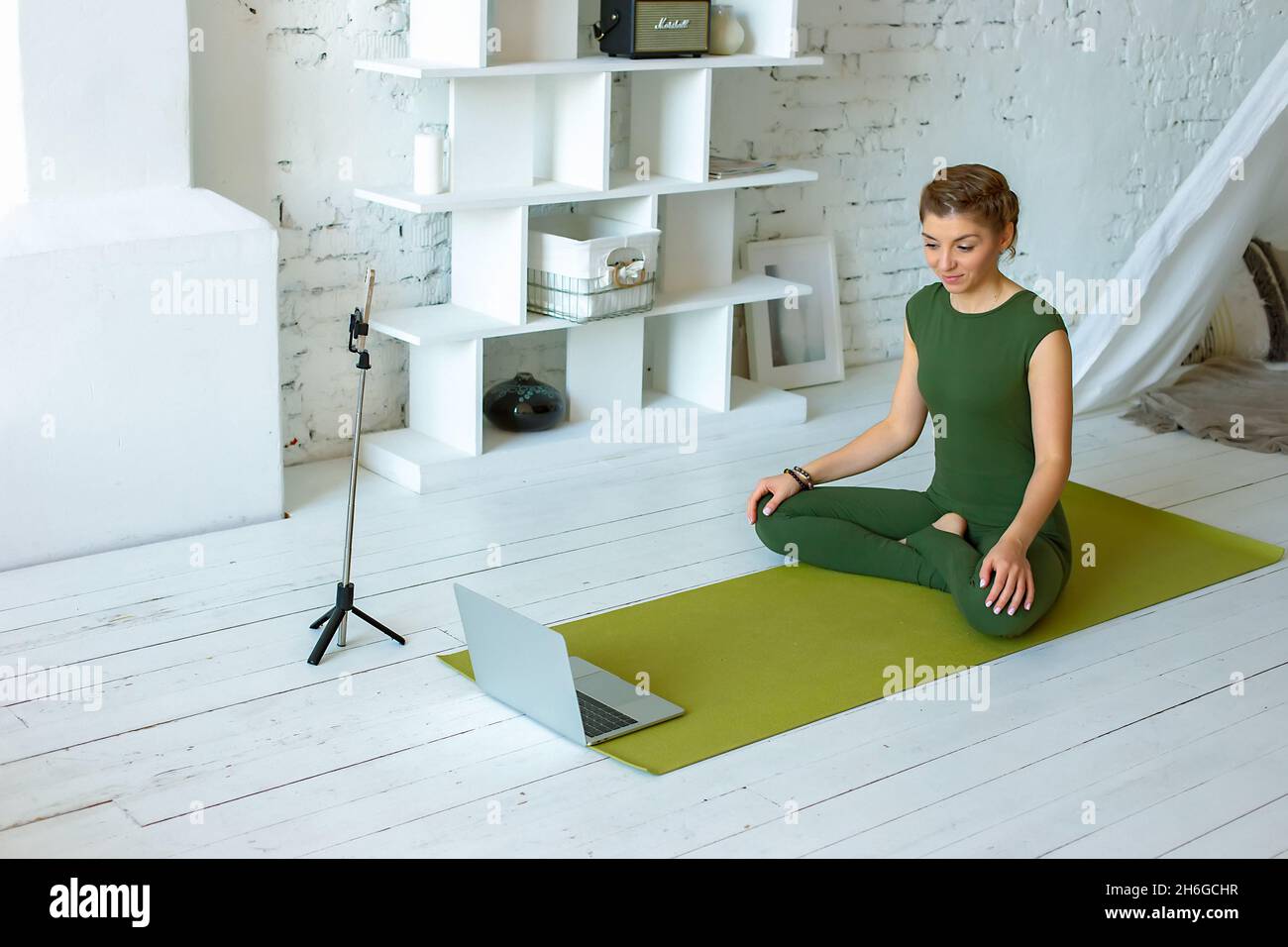 Una donna bella e sottile in abbigliamento sportivo verde scrive le lezioni di yoga a casa Foto Stock