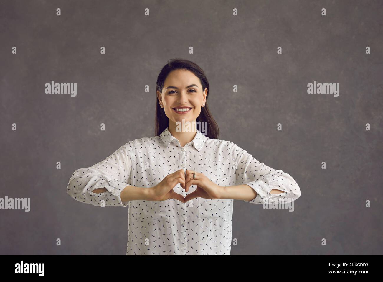 Bella donna amichevole esprime un gesto d'amore in piedi su uno sfondo grigio. Foto Stock