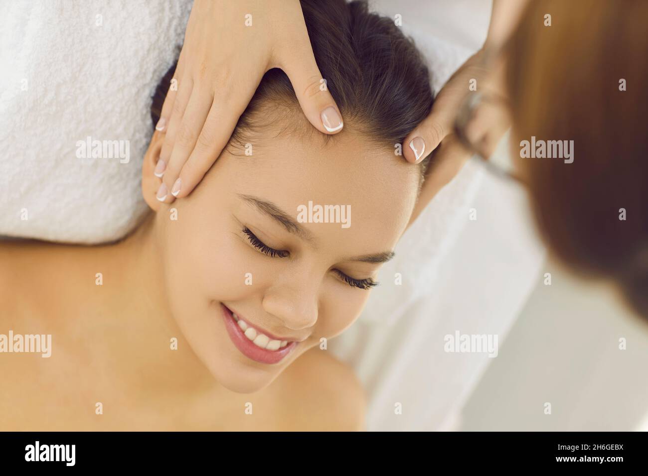 La cliente felice femmina gode di massaggio facciale da massaggiatore professionale in ufficio della spa moderna. Foto Stock