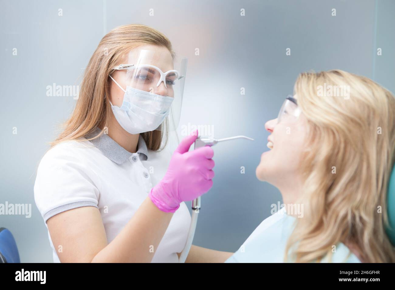 Dentista femminile che indossa maschera medica e visiera protettiva in plastica, che lavora con la paziente durante la pandemia di coronavirus Foto Stock