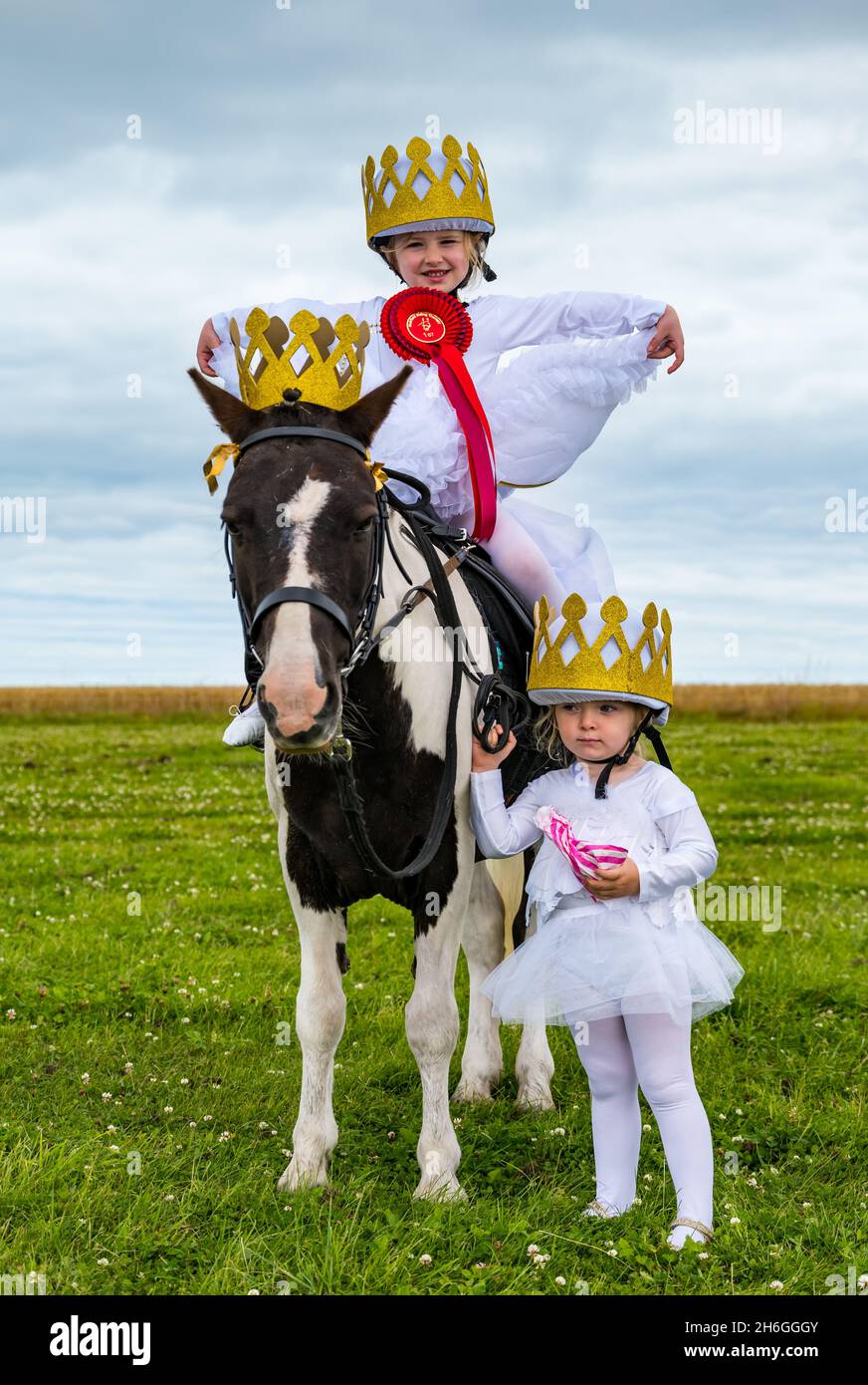 Spettacolo estivo di cavalli: Due giovani ragazze, sorelle, con corone con un pony con 1° posto rosetta in un concorso di abbigliamento fantasia, East Lothian, Scozia Foto Stock