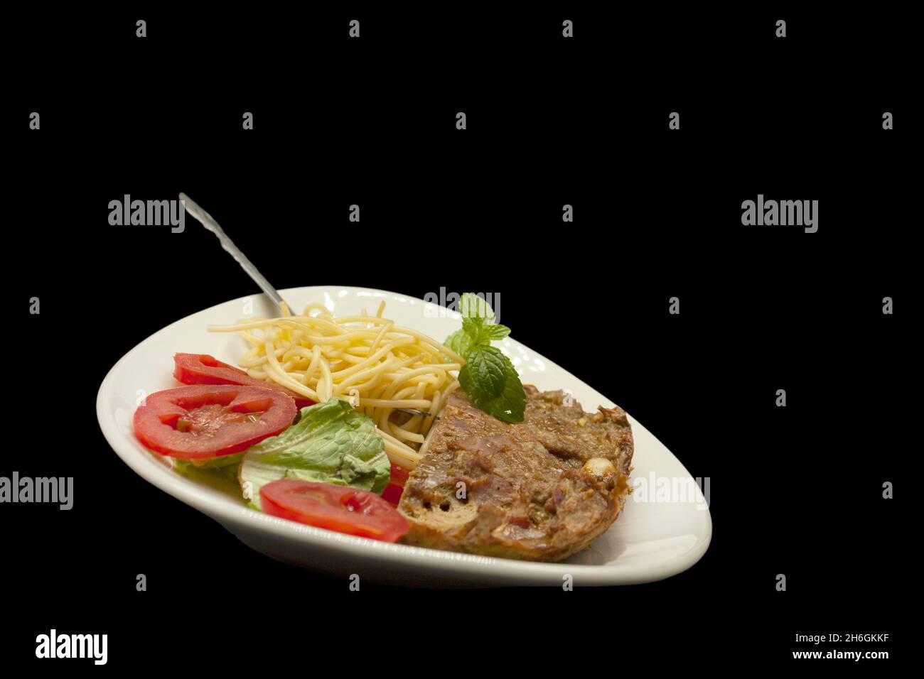 torta di carne accompagnata da spaghetti, lattuga e insalata di pomodoro guarnita con menta servita in un piatto ovale Foto Stock