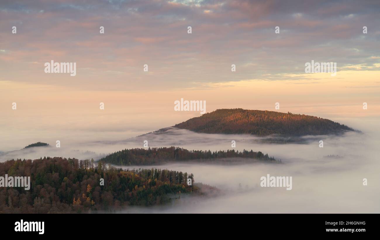 I primi raggi solari colpiscono la cima di una montagna avvolta nella nebbia Foto Stock