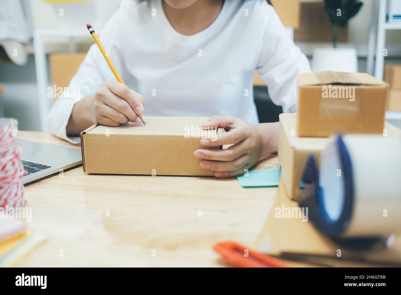 Closeup mano di giovane donna che scrive l'indirizzo sulla scatola del pacco per l'ordine di consegna al cliente, la spedizione e la logistica, il commerciante in linea e il venditore, il commercio Foto Stock