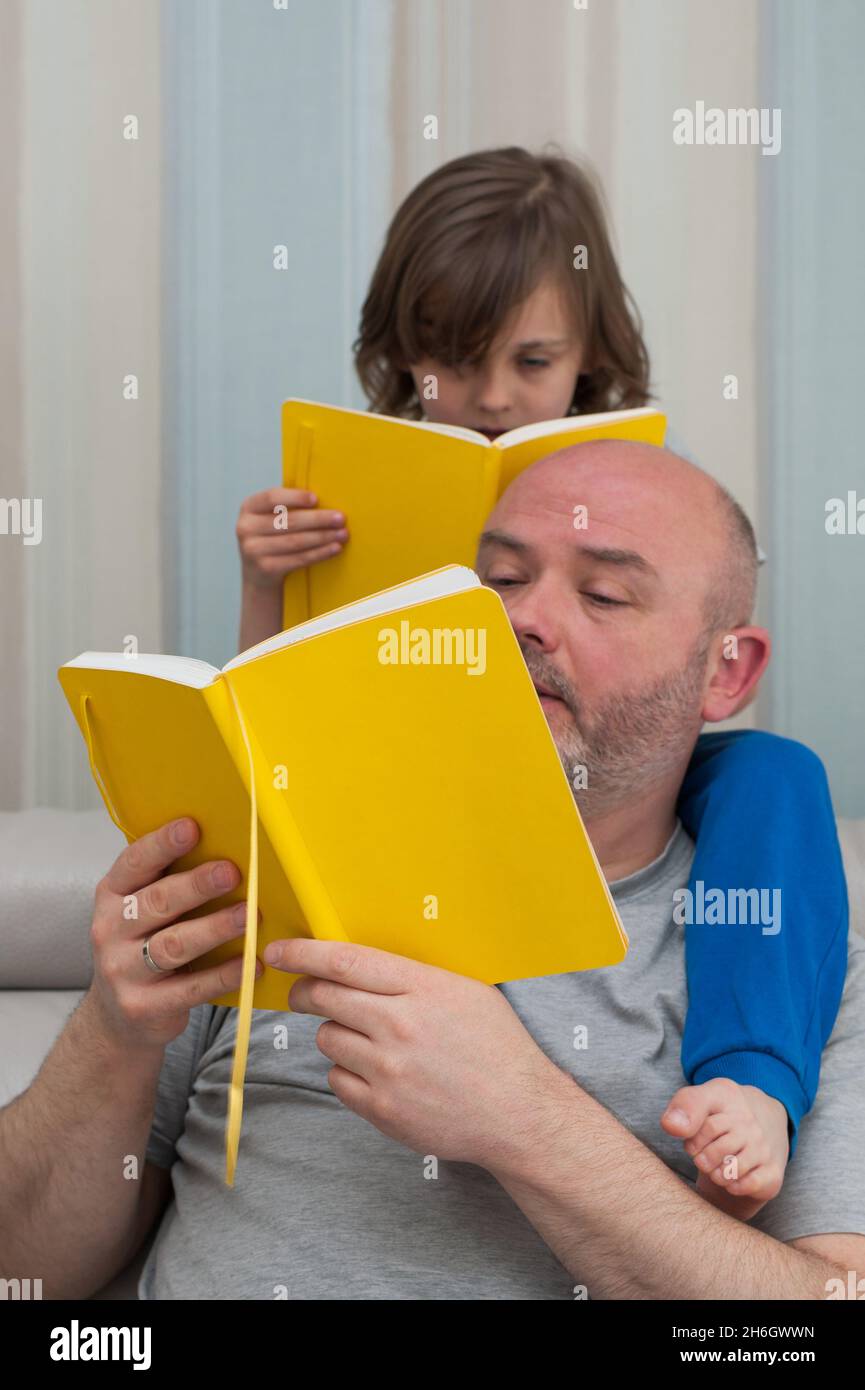 Padre e figlio insieme godendo di leggere e discutere gli esercizi di compiti scolastici da libro di testo giallo. Foto Stock