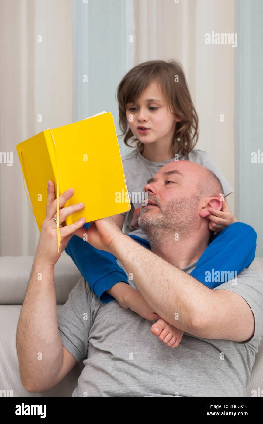 Padre e figlio insieme godendo di leggere e discutere gli esercizi di compiti scolastici da libro di testo giallo. Foto Stock