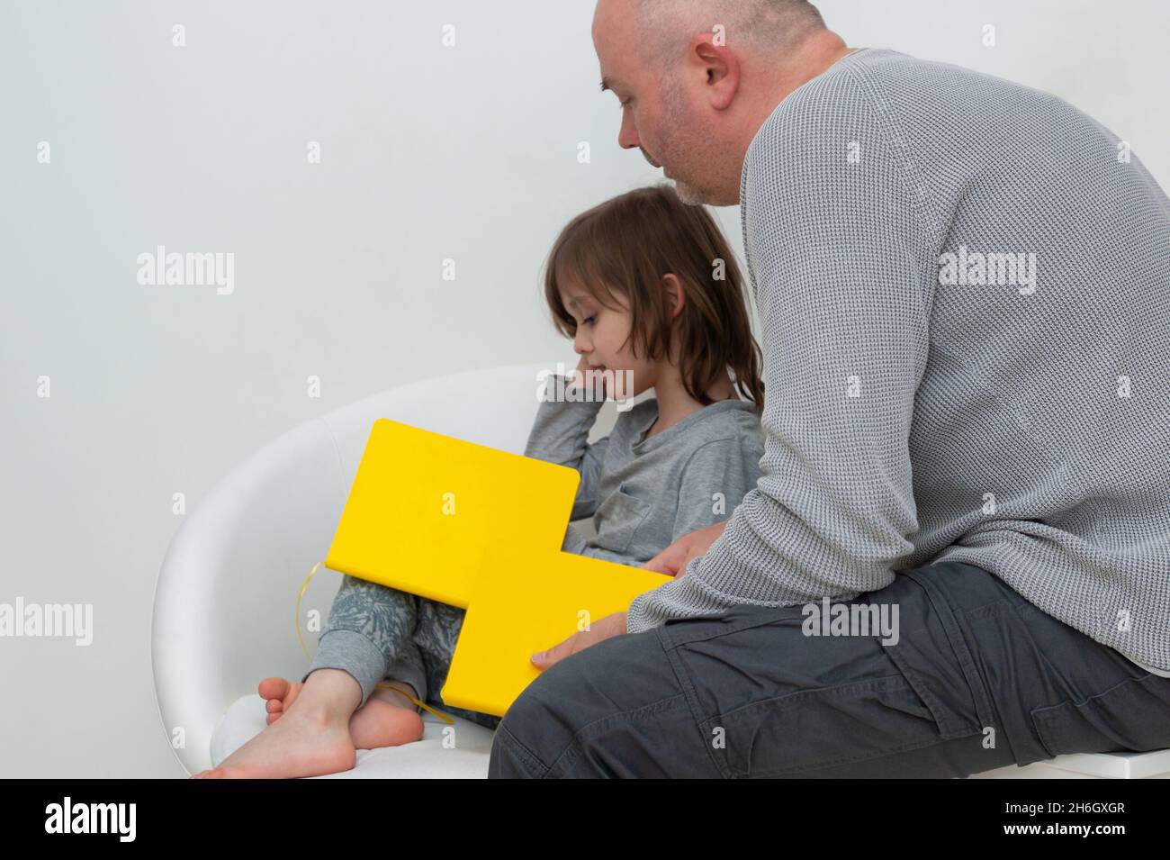 Padre e figlio insieme godendo di leggere e discutere gli esercizi di compiti scolastici da libro di testo giallo. Foto Stock