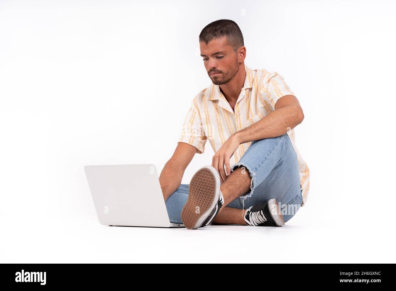 Giovane uomo seduto a terra con il suo computer portatile Foto Stock