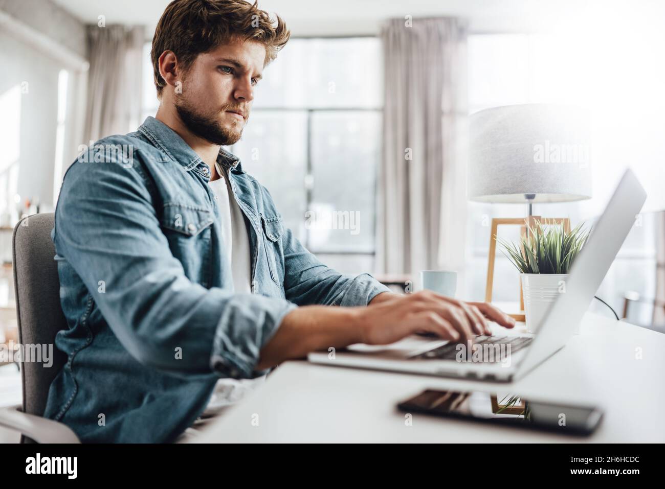 Giovane uomo che digita su un portatile. Uomo d'affari moderno in ufficio soleggiato. Freelance al lavoro. Blogger o giornalista che scrive nuovo articolo Foto Stock