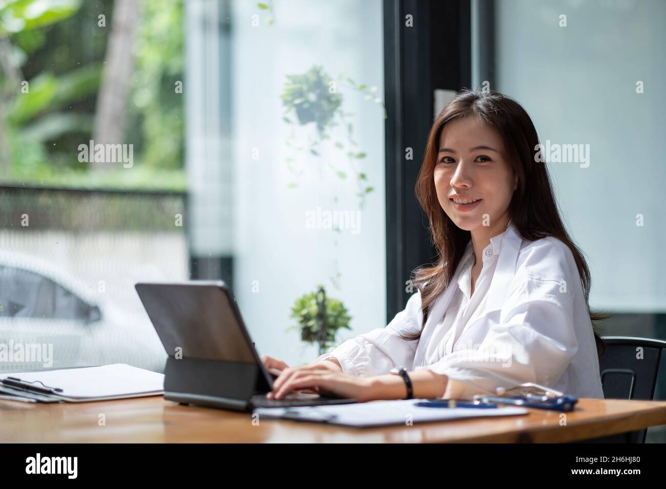 Medico donna asiatica con stetoscopio seduto e utilizzando il computer portatile per controllare l'elenco dei pazienti. Come consultazione giovane signora ha successo lavoro da molti positivi Foto Stock