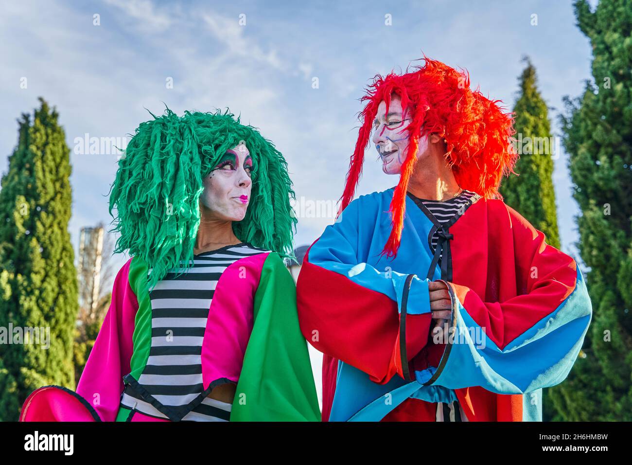 Positivo harlequins maschio e femmina con volti dipinti in costumi e parrucche colorati, sorridendo e guardando l'un l'altro durante il festival in Ark in giorno di sole Foto Stock