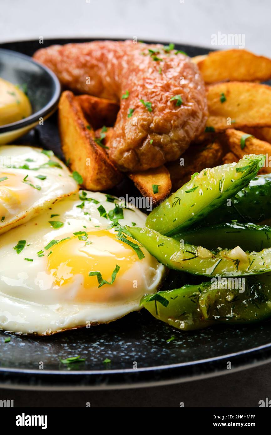 Primo piano di vista delle uova fritte con salsiccia, spicchi di patate e cetriolo sottaceto Foto Stock