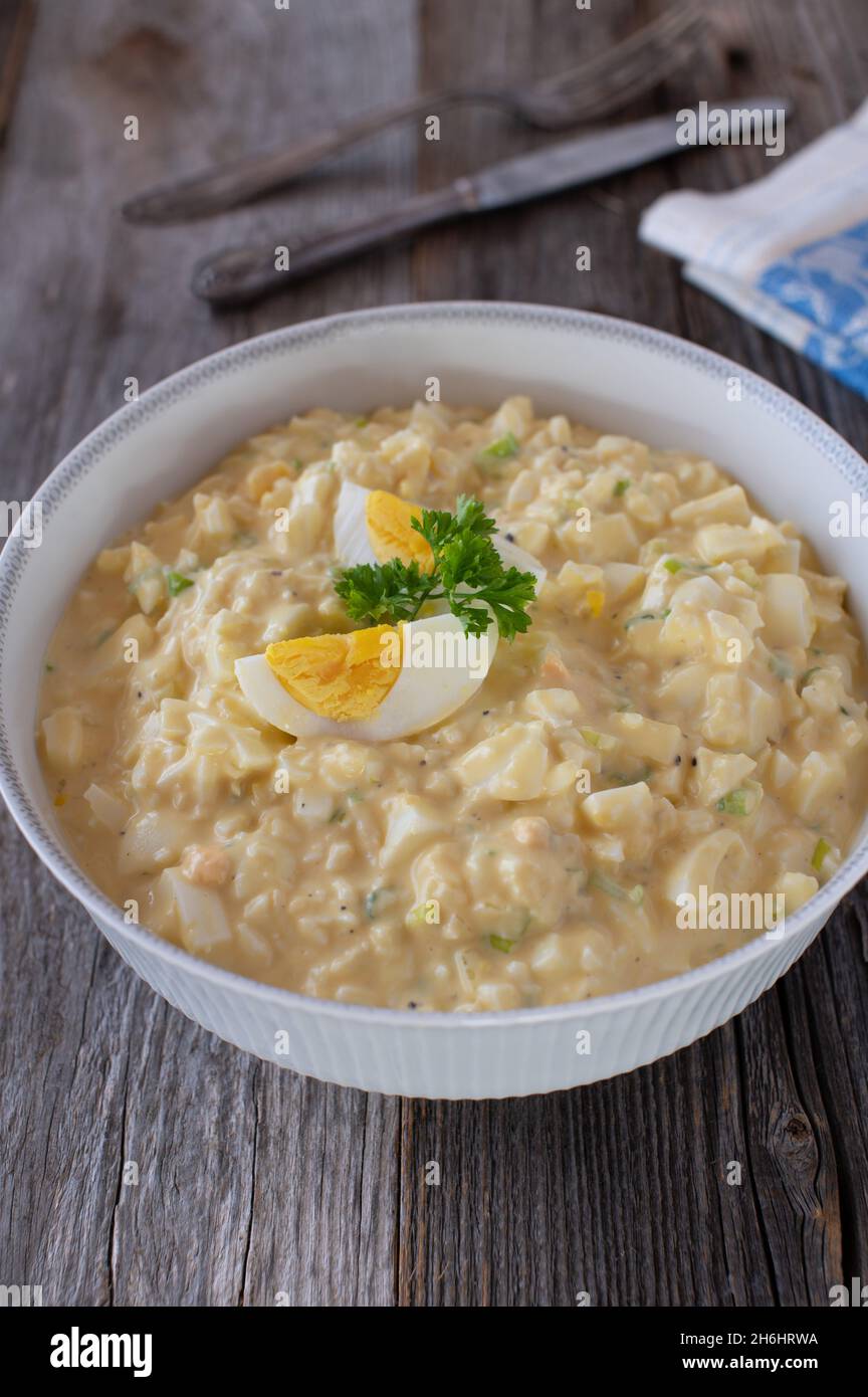 Ciotola con insalata di uova tradizionale fatta in casa e fresca isolata su tavola di legno. Immagine verticale Foto Stock