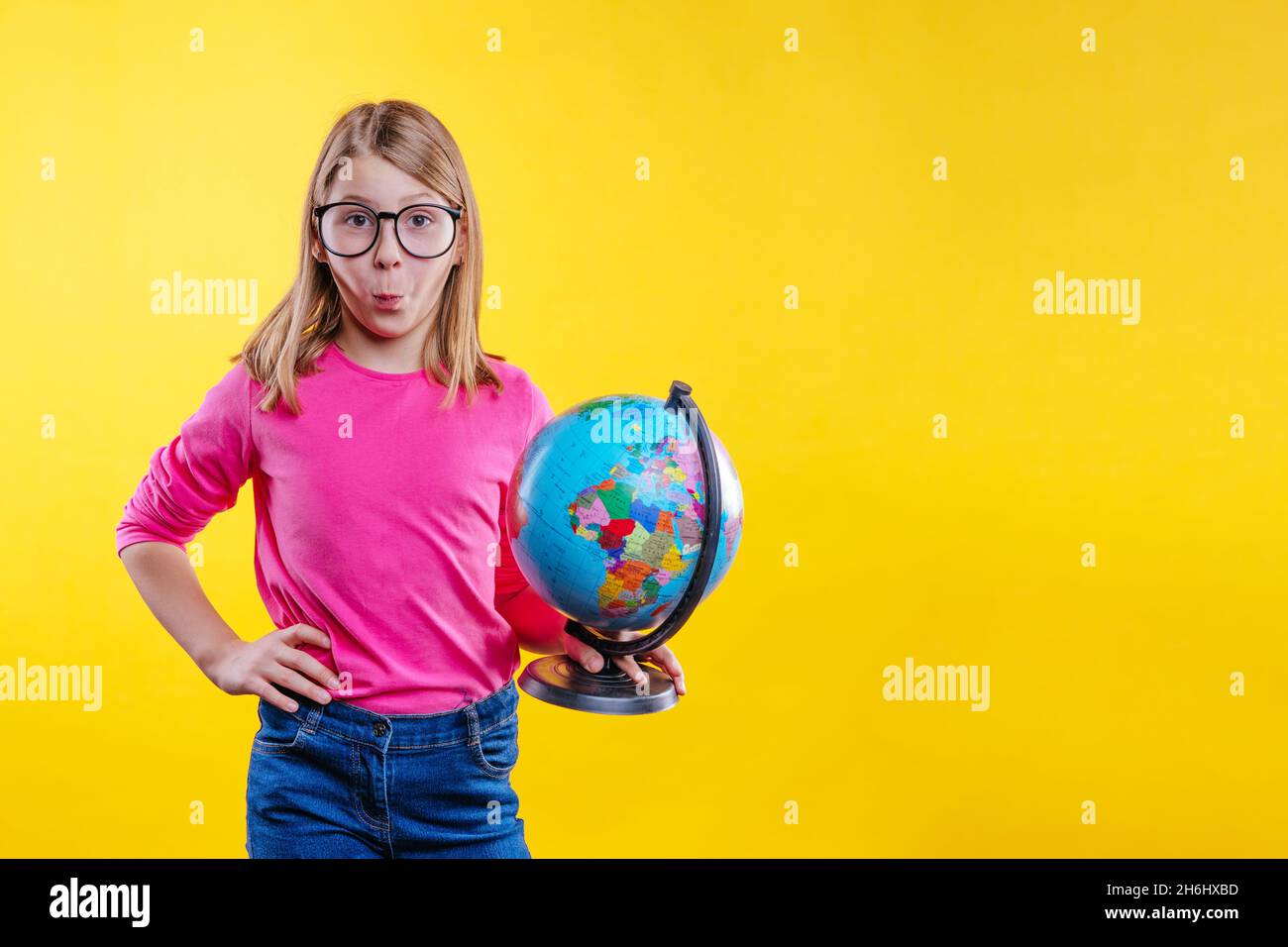 Studentessa bionda sorprendo con occhiali che tengono il globo su sfondo giallo con spazio vuoto per il testo Foto Stock