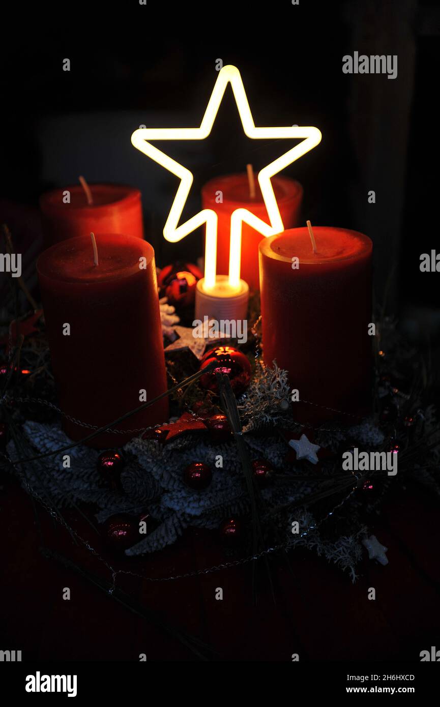 Decorazioni natalizie all'interno. Una corona d'avvento con quattro candele rosse e una stella d'illuminazione in un'oscurità Foto Stock