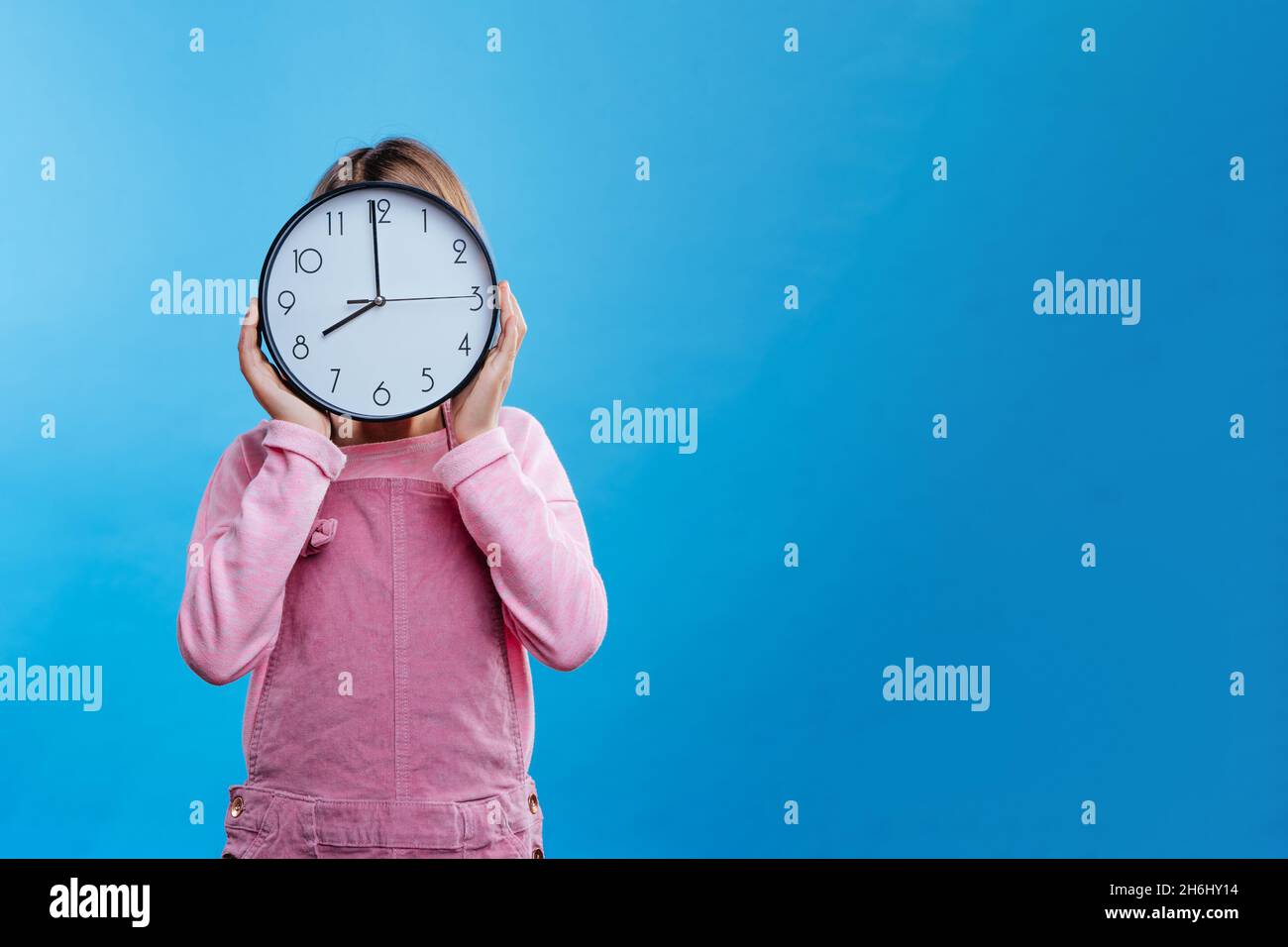 Bambina che tiene l'orologio su sfondo blu con spazio vuoto per il testo. Banner panoramico orizzontale. Foto Stock