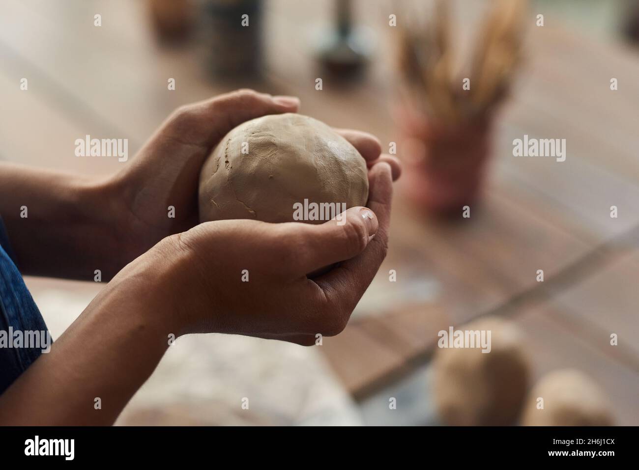Mani di giovane donna che tengono pezzo sferico di argilla impastata sul posto di lavoro mentre si va a fare terracotta Foto Stock