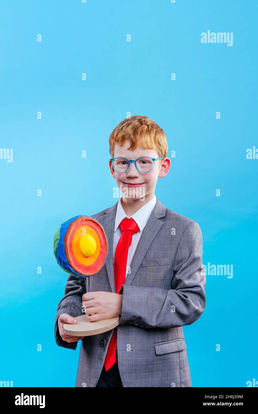 Il ragazzo che indossa il vestito e la cravatta con gli occhiali che tengono la sua sezione scientifica del progetto della Terra su sfondo blu con spazio vuoto per il testo Foto Stock