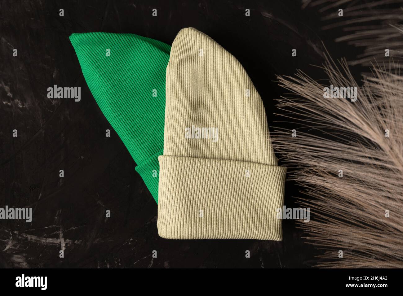 Cappelli di beanie verdi e pistacchio su sfondo scuro con fiori secchi. Foto Stock