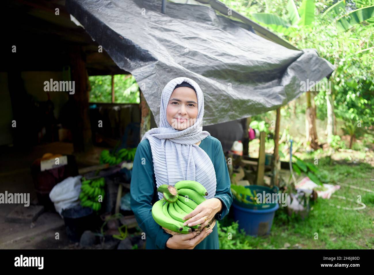 Donna musulmana in piedi hijab e tenendo la banana cruda in casa Foto Stock