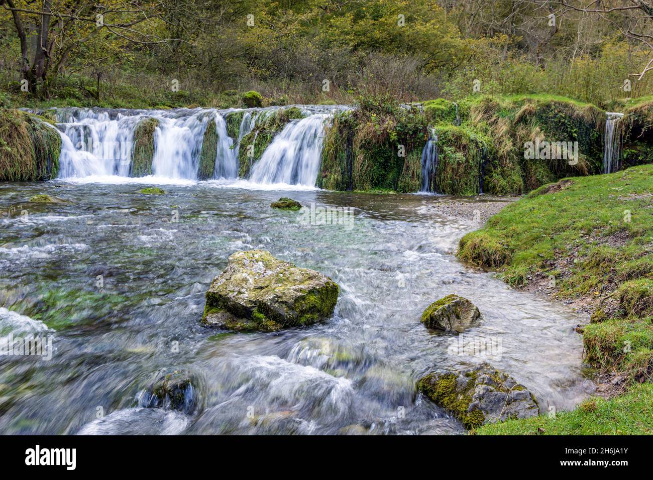 Tufa Dam o weir è una cascata pittoresca su rocce calcaree, fiume Lathkill, Lathkill Dale, Peak District National Park, Derbyshire, Inghilterra. Foto Stock
