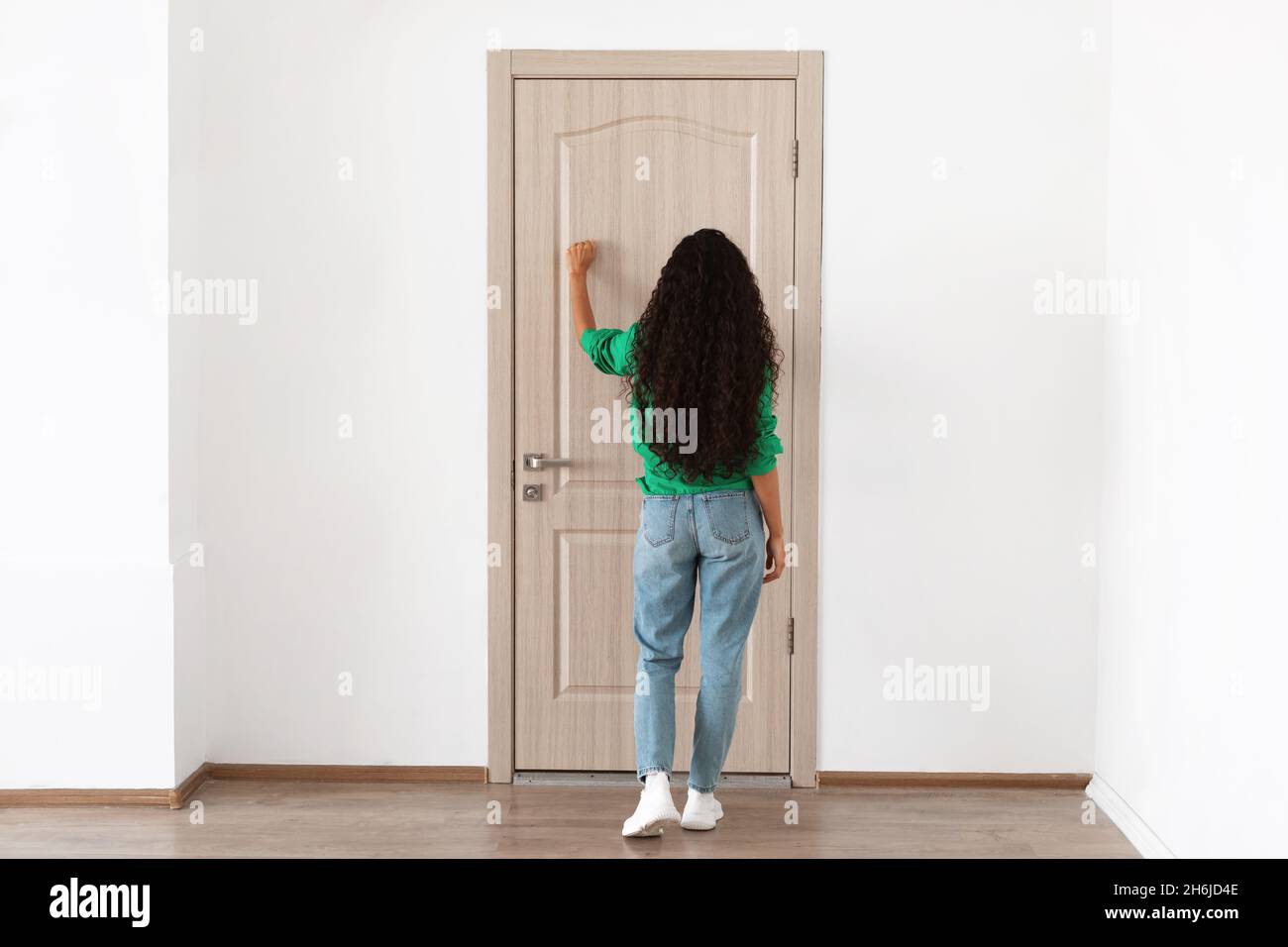 Vista posteriore della donna che bussa alla porta di legno Foto Stock