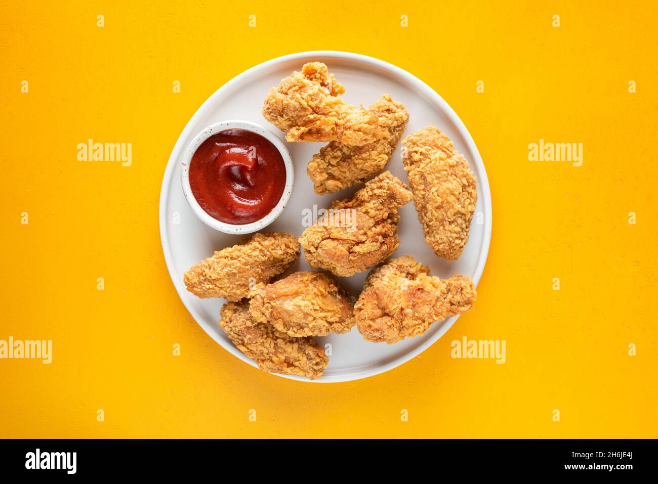 Ali di pollo fritte profonde sul piatto isolato su sfondo giallo vista dall'alto Foto Stock
