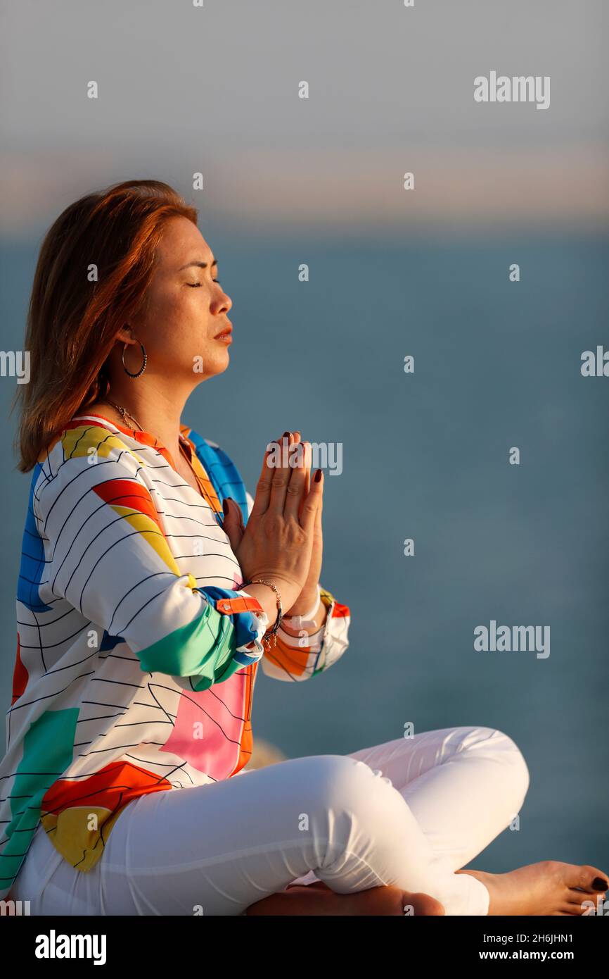 Donna che pratica la meditazione yoga sul mare prima del tramonto come concetto di silenzio e relax, Emirati Arabi Uniti, Medio Oriente Foto Stock