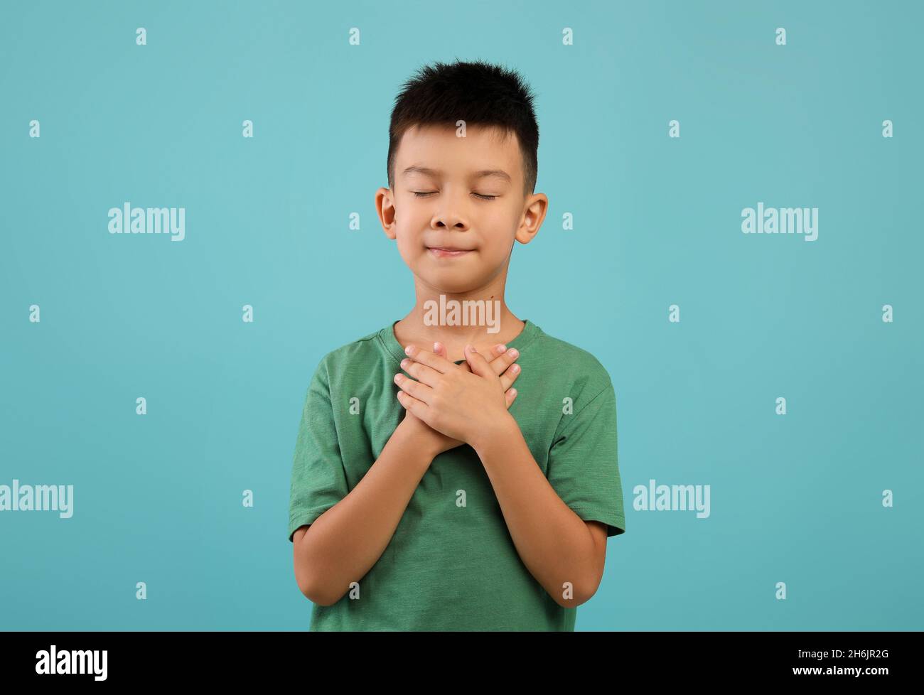 Concetto di gratitudine. Thankful piccolo ragazzo asiatico mantenendo entrambe le palme sul Chest Foto Stock