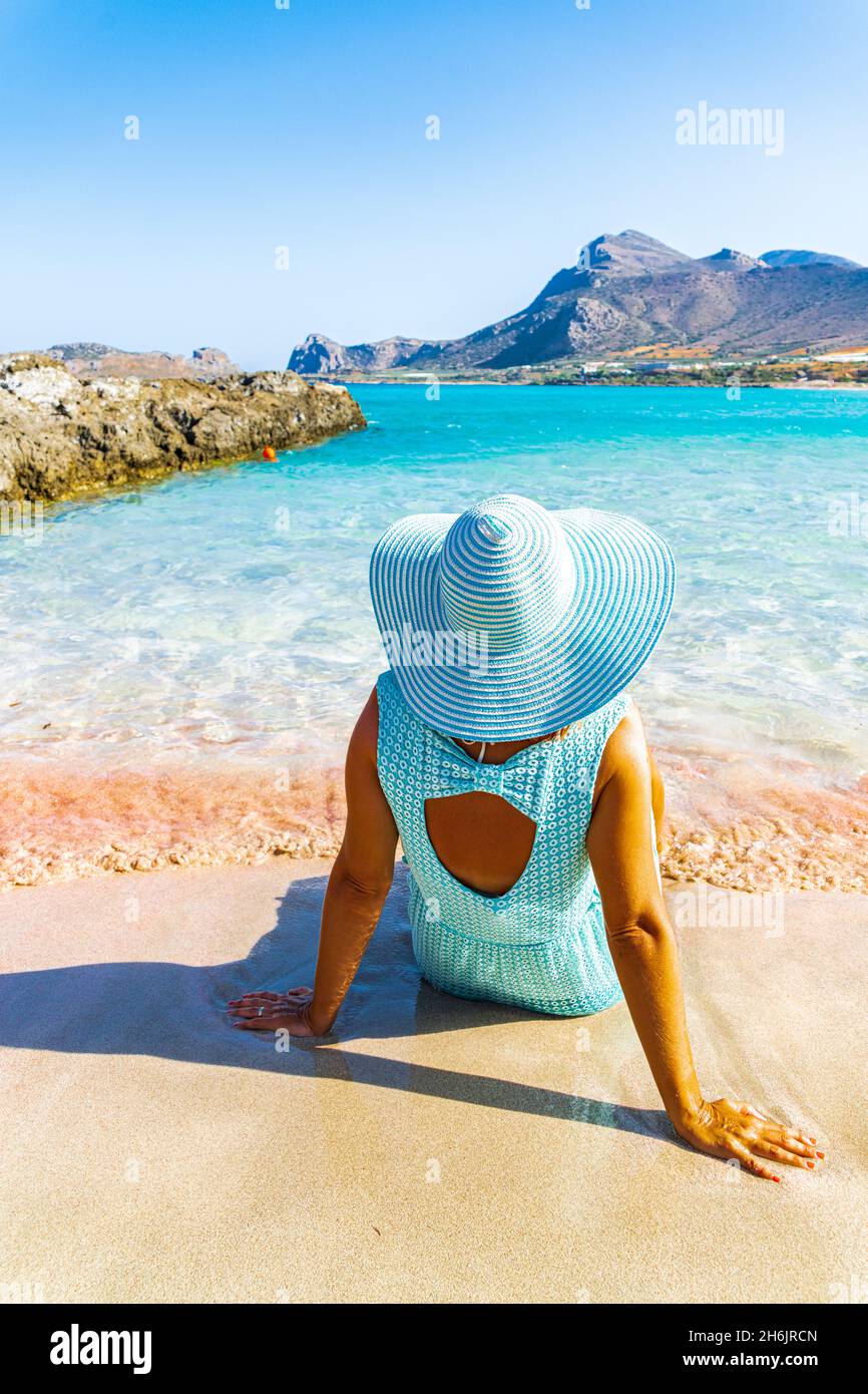 Vista posteriore della donna che contempla il mare seduto sulla sabbia rosa della spiaggia di Falassarna, Kissamos, la Canea, Creta, Isole Greche, Grecia, Europa Foto Stock