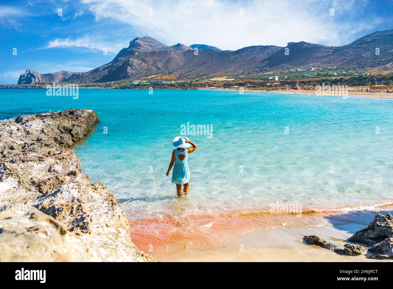 Donna in abito in piedi nel mare turchese chiaro di fronte alla spiaggia di sabbia rosa di Falassarna, Creta, Isole Greche, Grecia, Europa Foto Stock