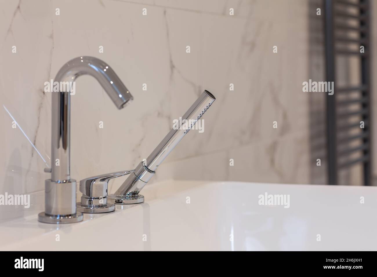 Immagine dettagliata del rubinetto del miscelatore per vasca e doccia cromata posizionata sulla testa di una vasca da bagno bianca Foto Stock