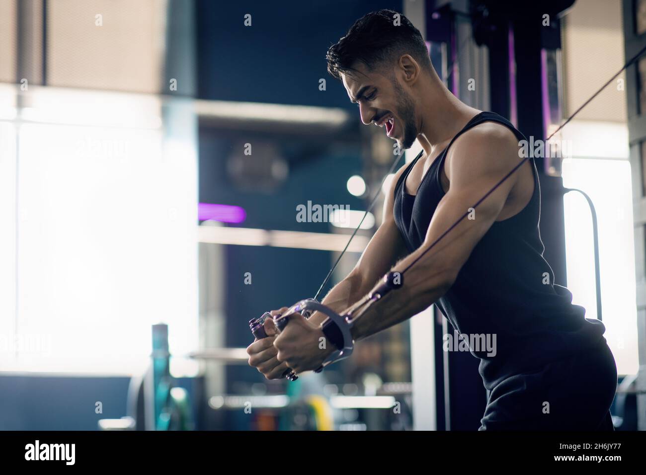 Giovane atleta maschile Medio Oriente allenamento triceps con Crossover Machine in palestra Foto Stock