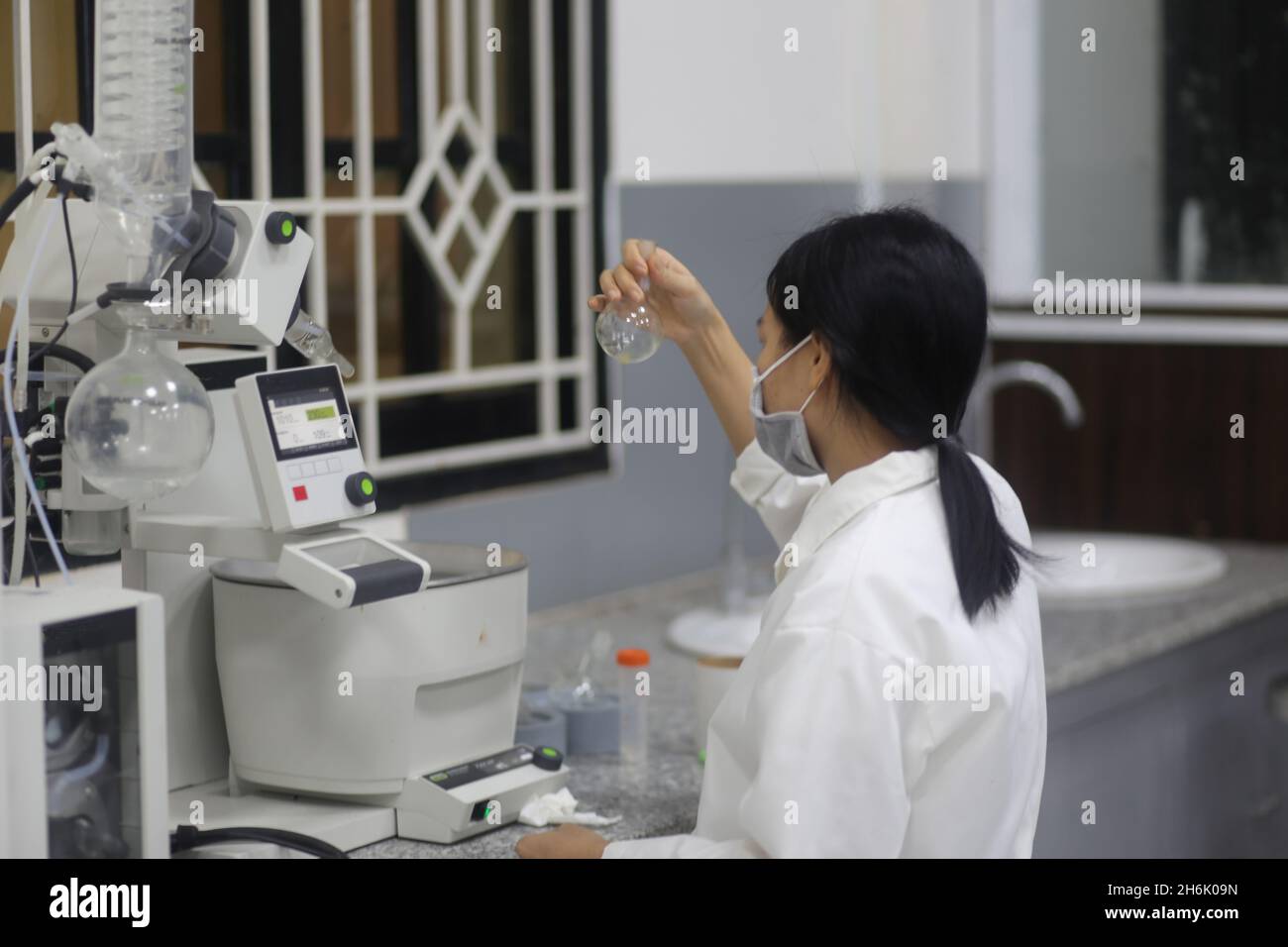 Donna vietnamita scienziato che controlla il pallone di vetro da laboratorio per fare un esperimento in laboratorio Foto Stock