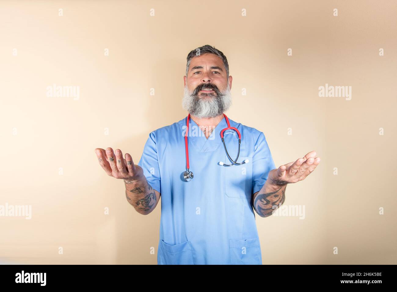 Ritratto di medico sorridente e gesturante mentre si trova in piedi contro parete background.Health lavoratori, covid-19, coronavirus e virus prevenzione concetto. Foto Stock