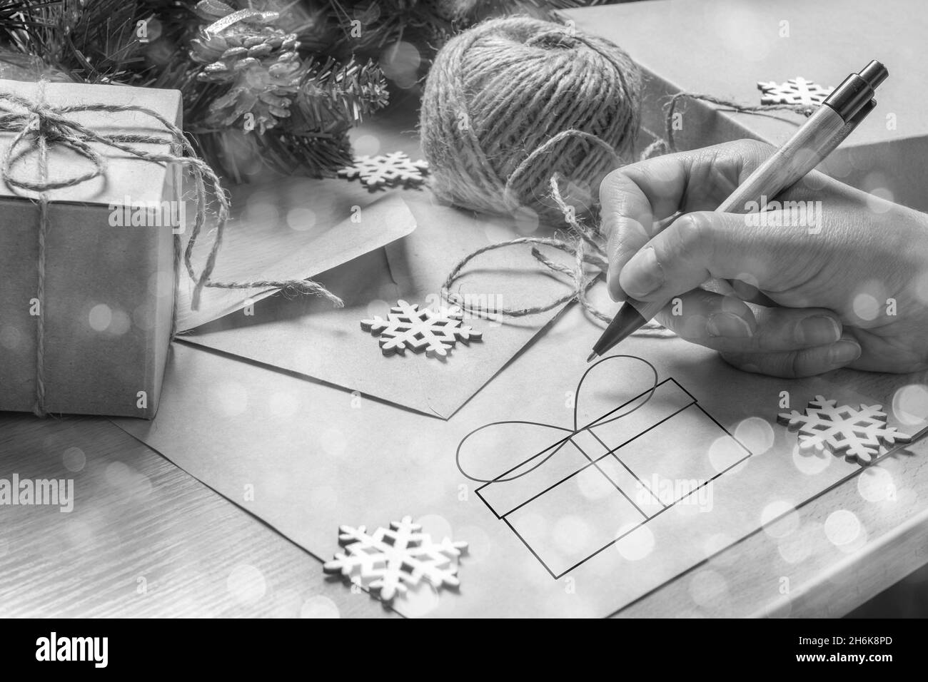 Donna a mano che scrive una lettera di Natale per Santa, disegnando una scatola del regalo sul tavolo con una busta, regali di Natale, albero di abete e fiocchi di neve, styl eco Foto Stock