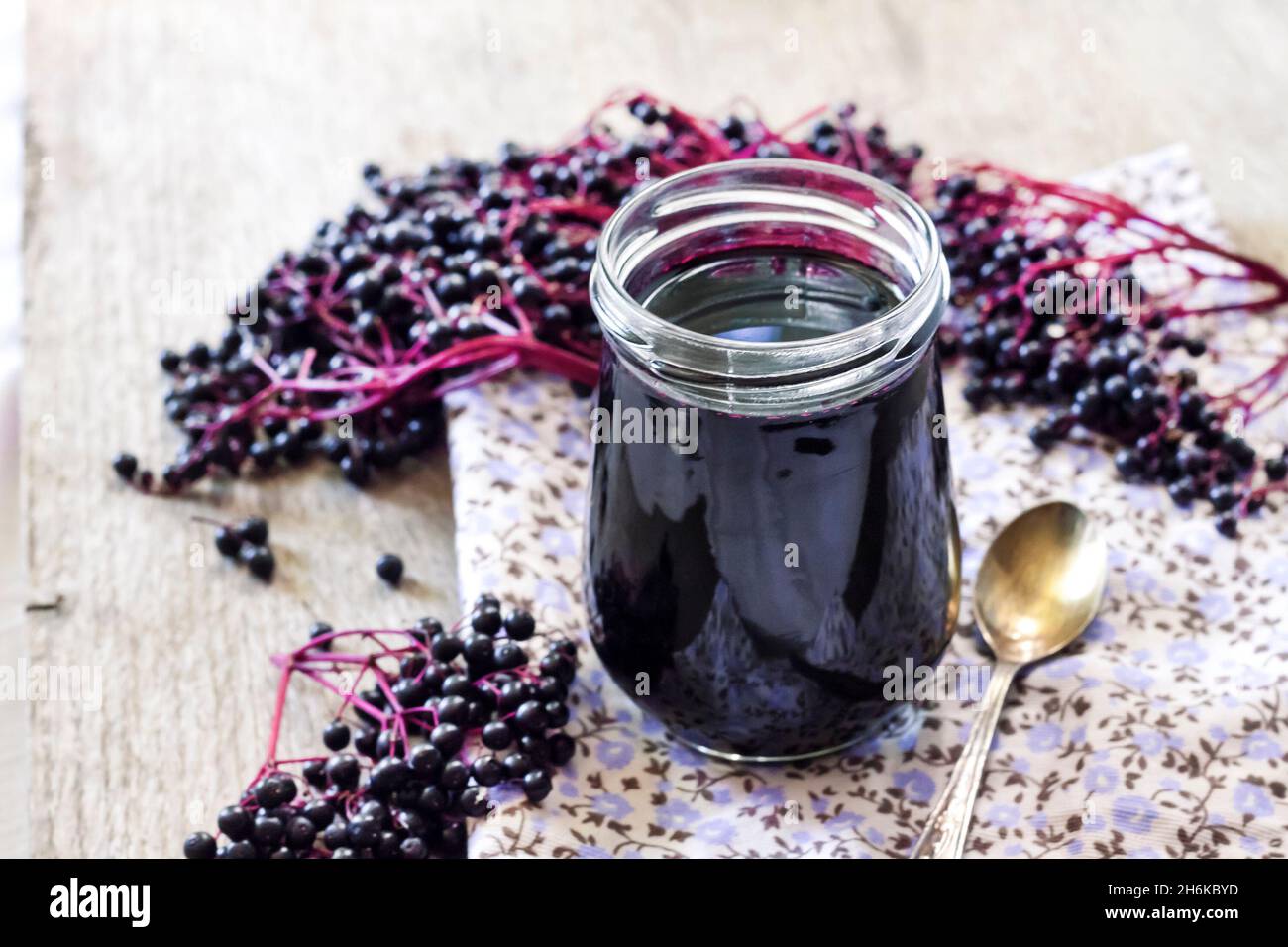 Sciroppo di sambuco nero fatto in casa in vaso di vetro e mazzi di sambuco nero sullo sfondo Foto Stock